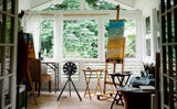 Black NatureWind Studio fan in a sunlit garden studio beside an easel