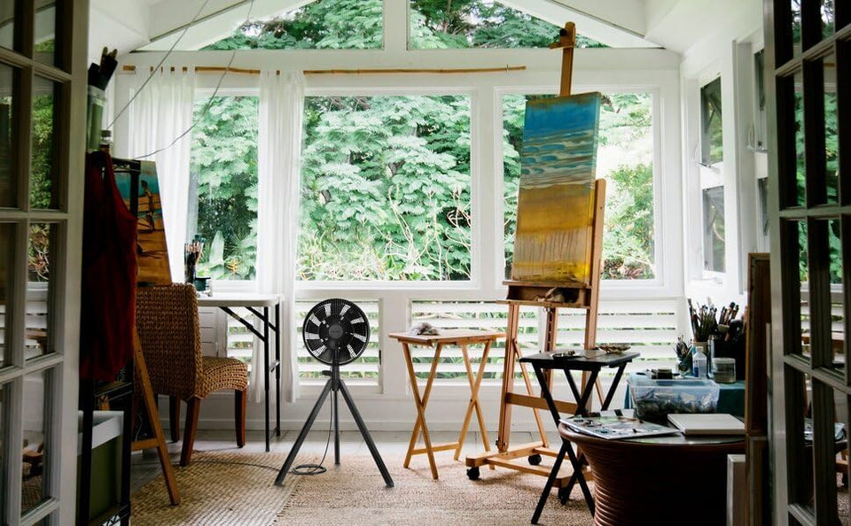 Black NatureWind Studio fan in a sunlit garden studio beside an easel