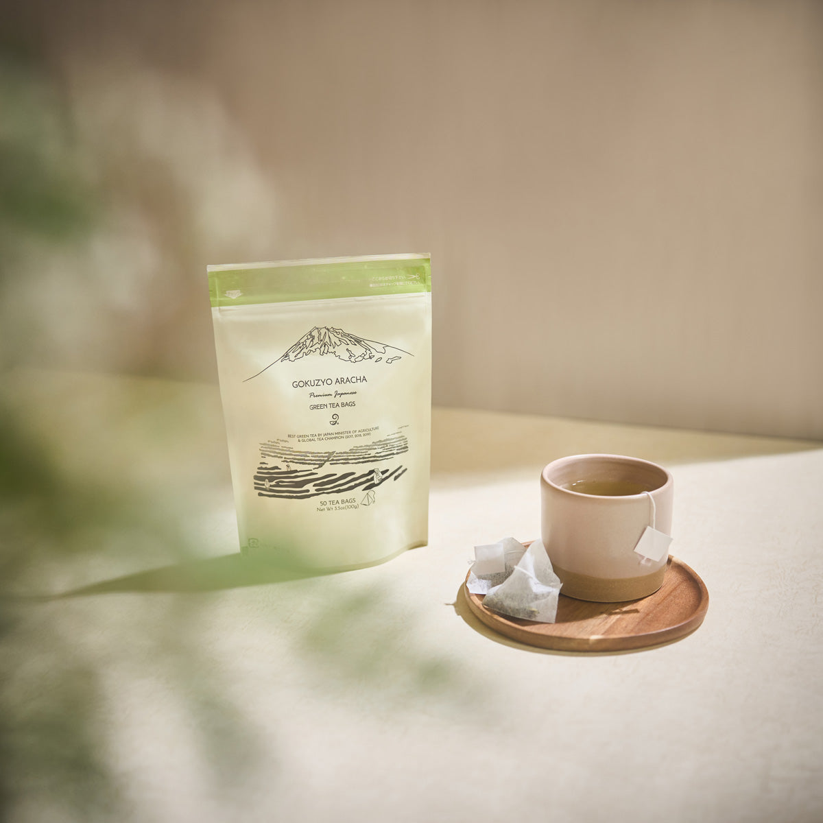 Gokuzyo Aracha tea bag pouch with a cup of brewed green tea and a tea bag on a wooden saucer