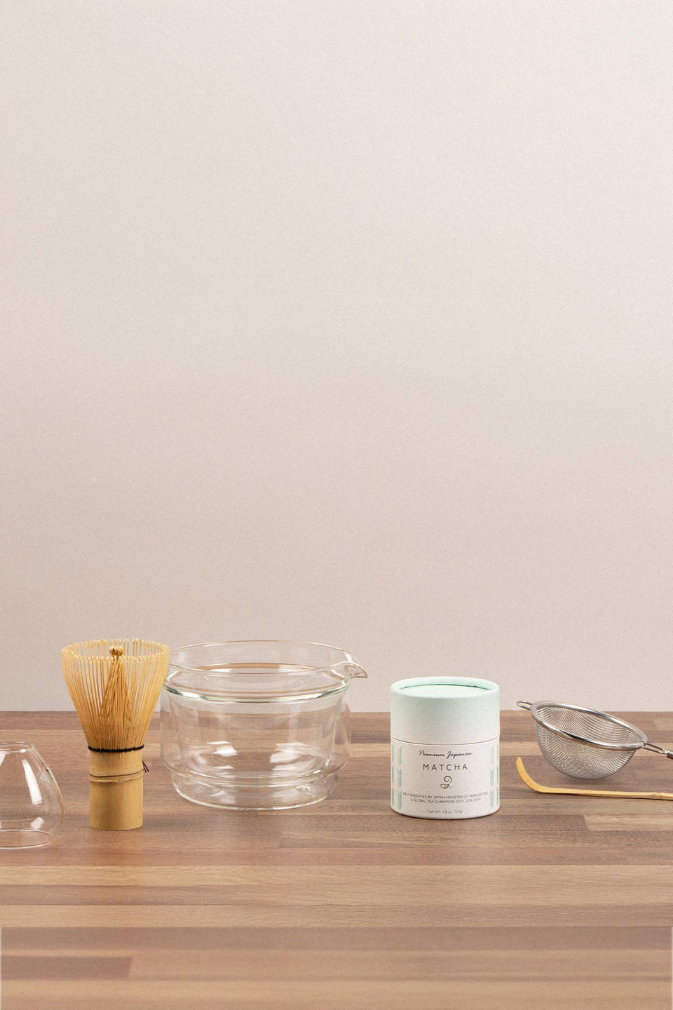 Tea-making tools including a whisk, bowl, and container on a wooden surface with a plain background