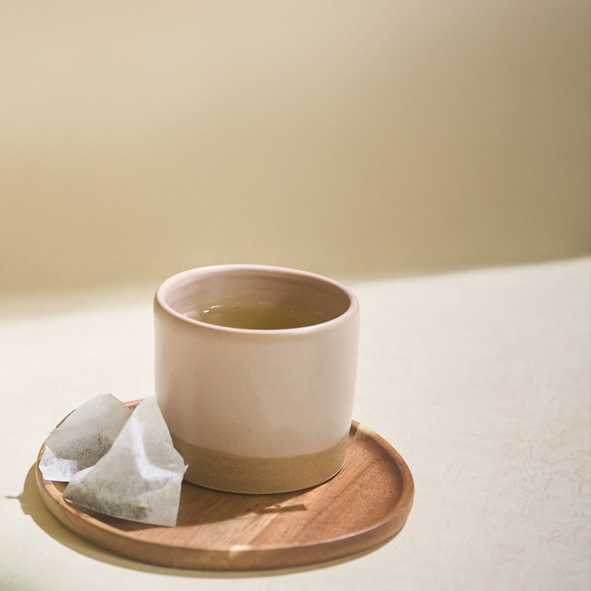 Cup of brewed Aracha green tea with a tea bag on a wooden saucer