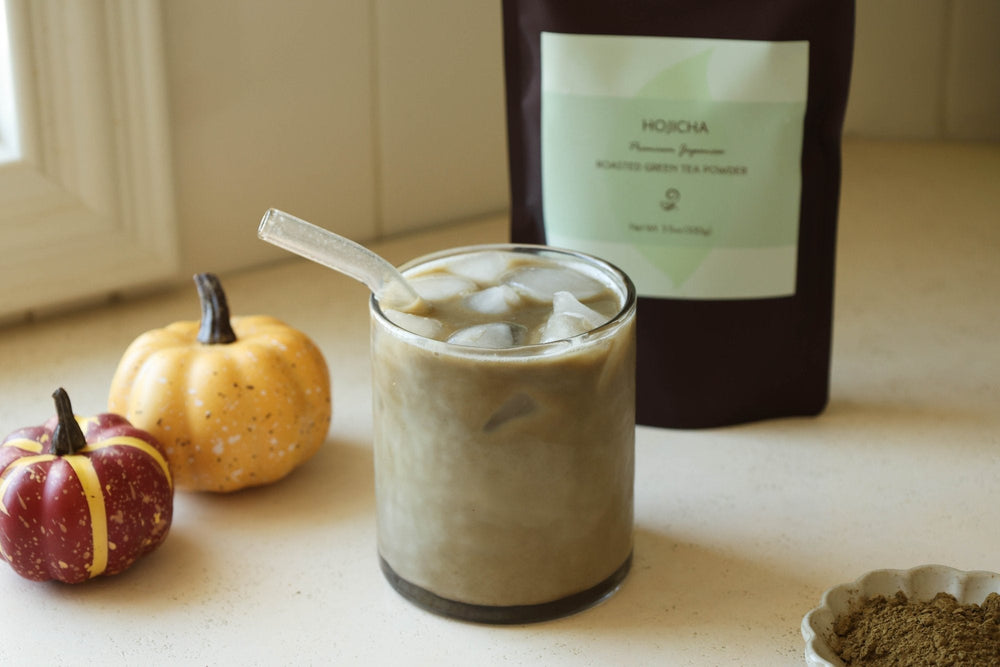 Iced pumpkin spice hojicha latte with small pumpkins and a bag of hojicha powder